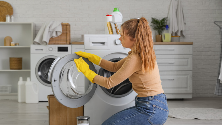 Person wearing yellow gloves cleaning a washing machine