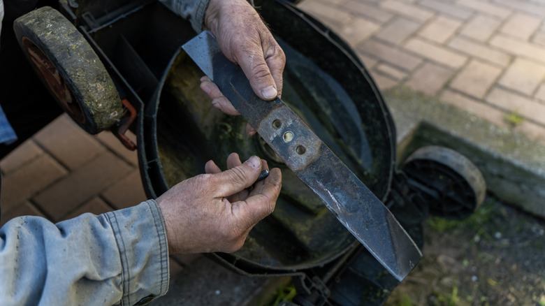 A person holding a lawn mower blade that's been removed from the mower deck