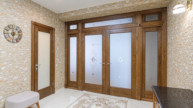 Well-lit entryway with stone-textured walls, wooden doors with frosted glass panels, and a patterned rug.