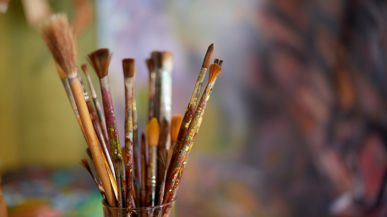 paintbrushes in jar by colorful painting