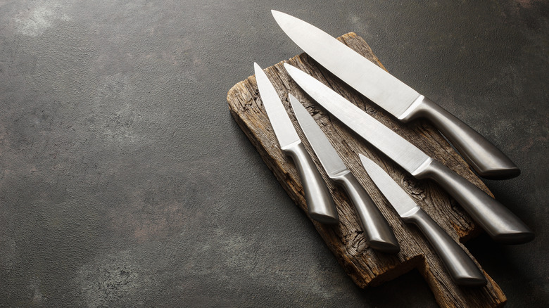 A variety of steel kitchen knives on a wooden cutting board