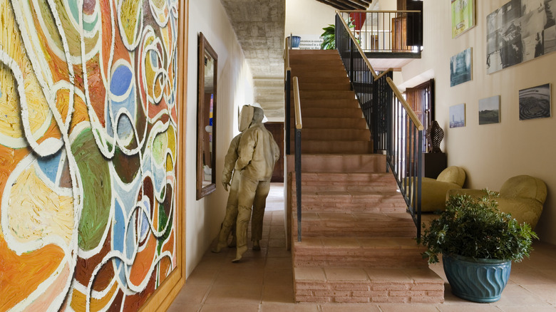 An eclectic assortment of art hangs on a wall near a staircase