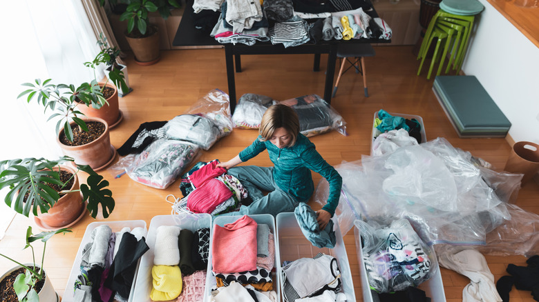 Woman sitting on the floor organizing, surrounded by bins of items