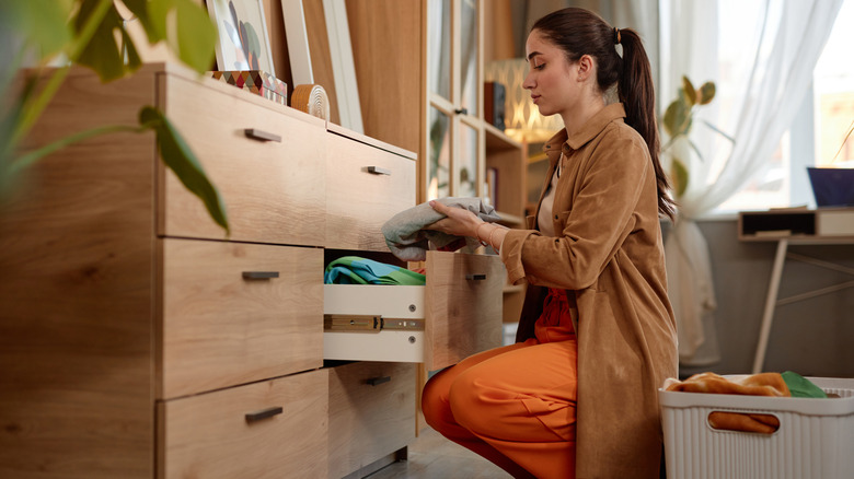 Woman in neat bedroom examining a folded item before placing in drawer