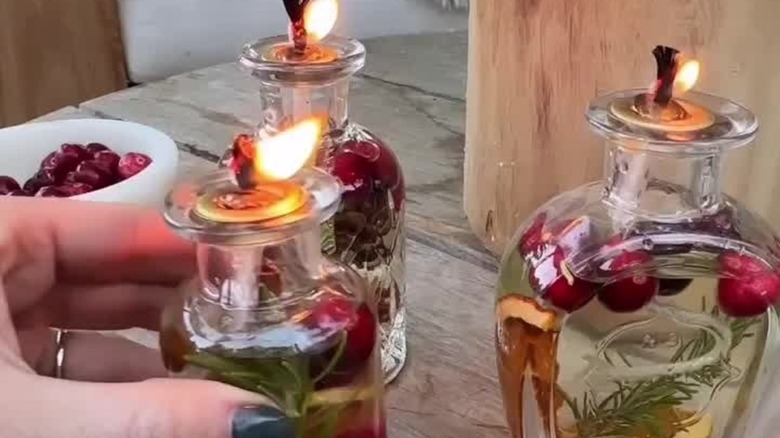DIY oil candles in glass jars filled with orange slices, pine sprigs, and cranberries