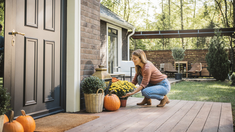 Young woman decorating her porch for fall with flowers and pumpkins