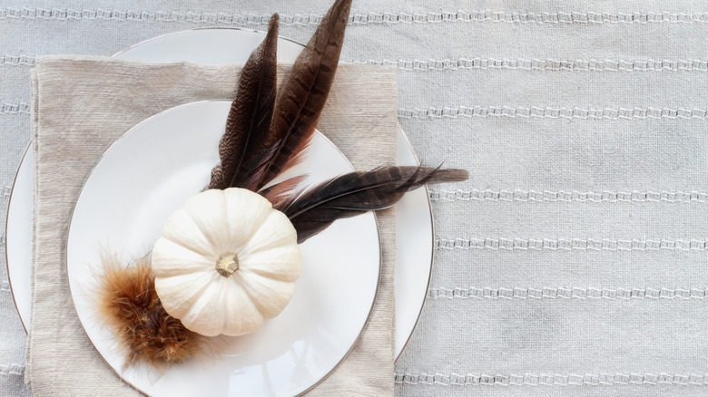 Fall table setting with decorative pumpkin and pheasant feathers on a plate