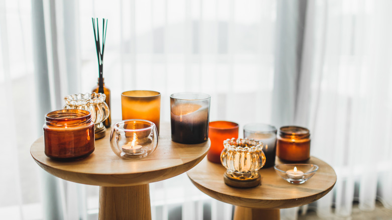 Organic soya wax candles in different glass candlestick in brown bowls on wooden tea-table near comfortable armchair.
