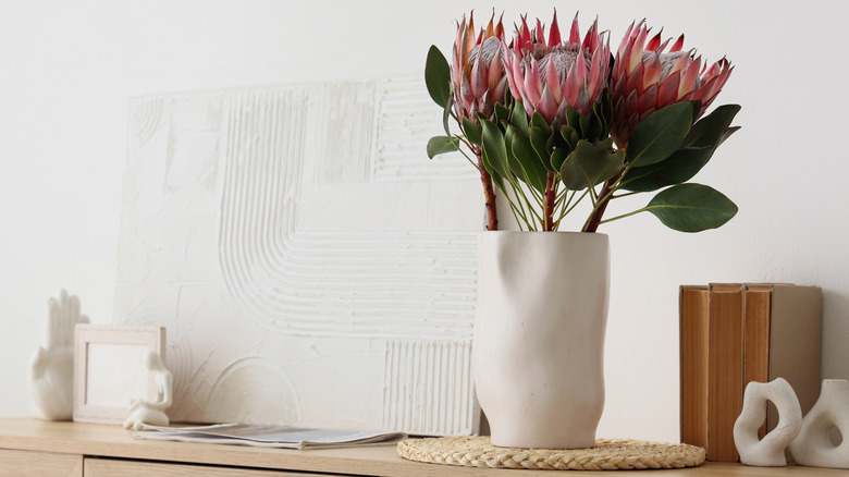protea flowers in a white vase next to white ceramic decor