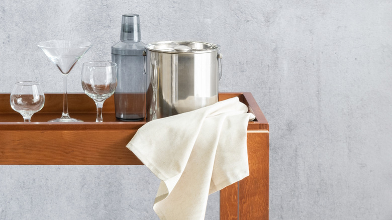 A wooden bar cart with shaker, glasses, and ice pale.