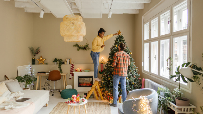 A couple decorates their apartment living room for Christmas.