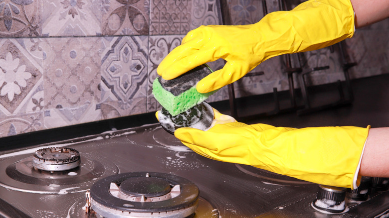Yellow gloved hand cleaning dirty gas stove top