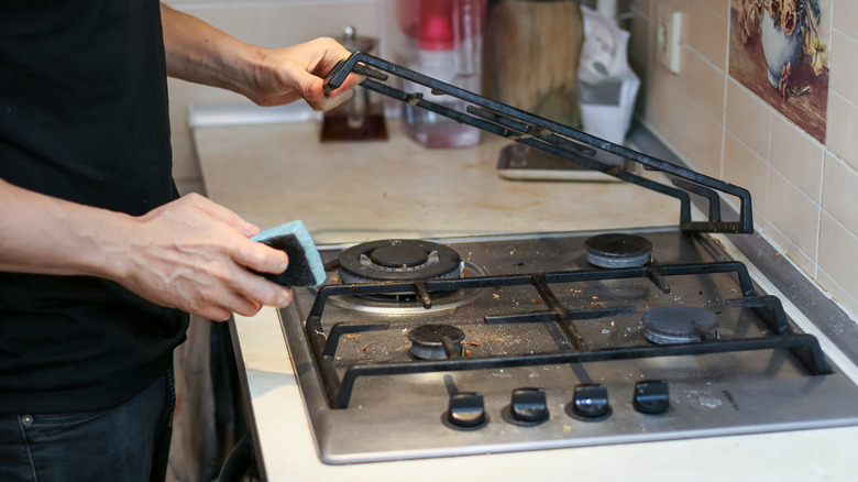 Man's hand cleaning under gas stove top grates