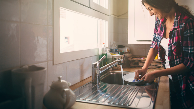 Woman washes dishes in sink