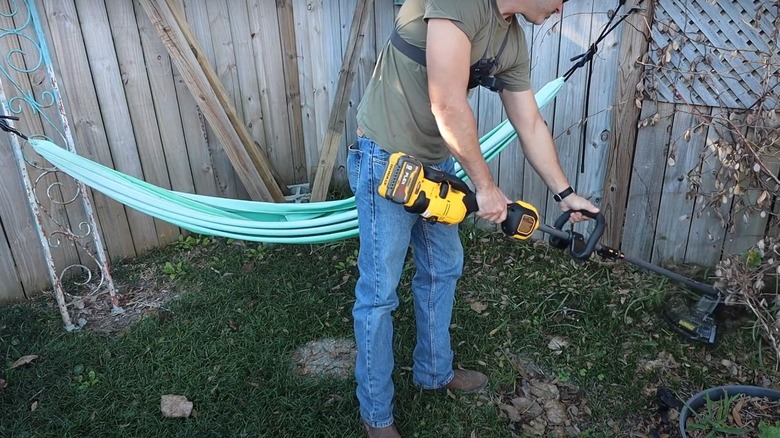 Man using a 60V DeWalt string trimmer near a fence