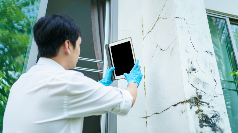 A person uses a tablet to document storm damage on the side of a house