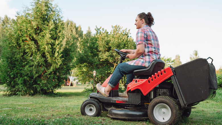 Woman mowing lawn with a red and black riding mower