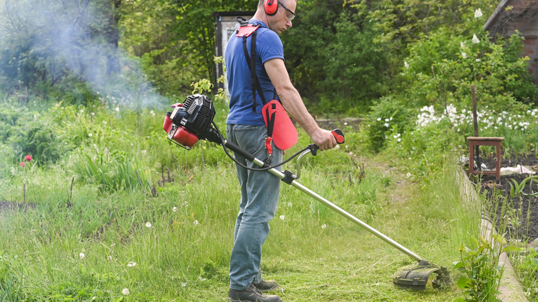 A man cutting grass with a gas-powered string trimmer