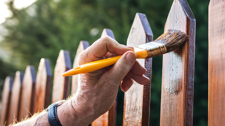 Person applying wood stain to a wood fence