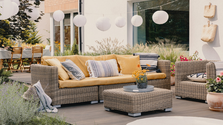 An inviting wicker patio set sits in front of a long table with wooden chairs