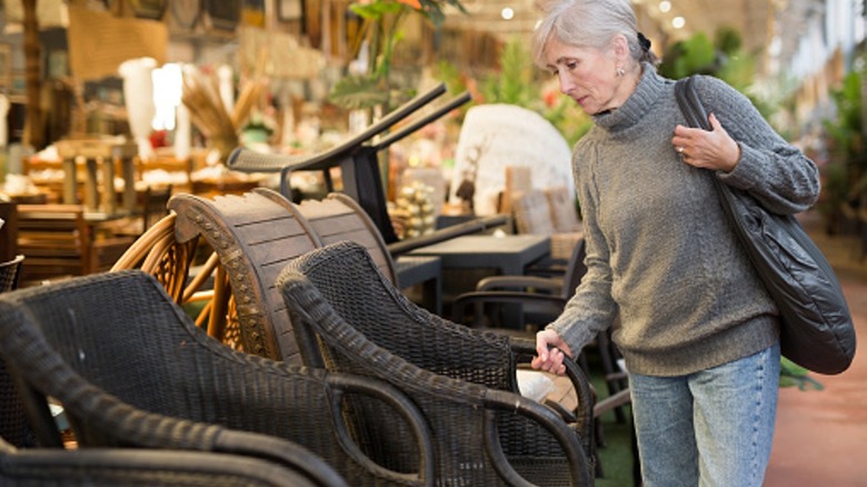 An elderly woman looks at a rattan patio chair on display