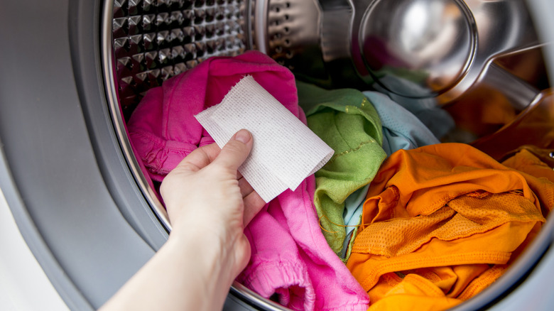 person putting dryer sheet into dryer filled with clothes