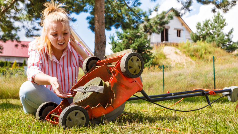 person trying to fix broken lawn mower in grassy yard