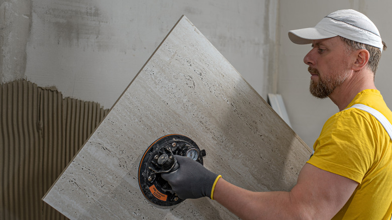 man uses suction handle to install large natural stone tile in bathroom