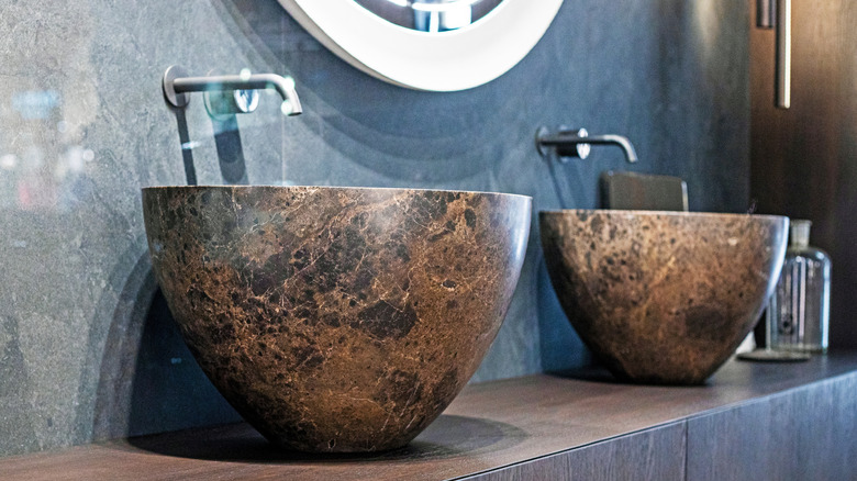 polished stone basins on wooden counter top against dark tiles in cave bathroom