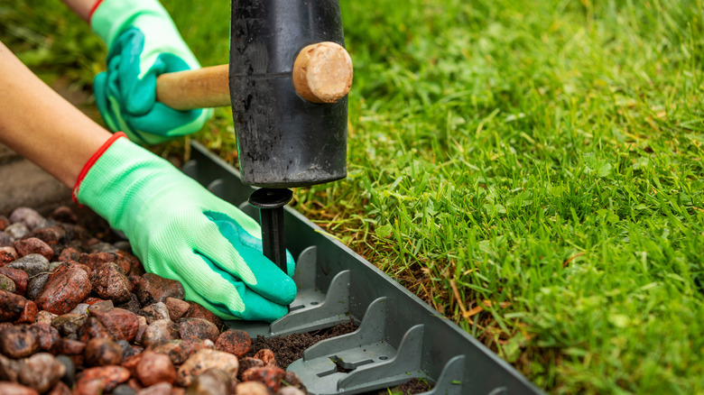 A person uses a rubber mallet to drive stakes into plastic paver edging