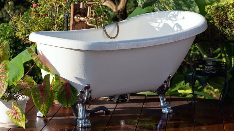 White bathtub on wooden platform outdoors surrounded by plants