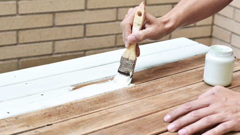 Man painting wooden slabs with white paint.