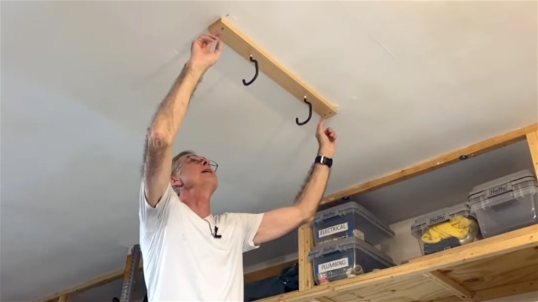 man installing DIY ceiling-mounted hanging hooks for long ladder rack
