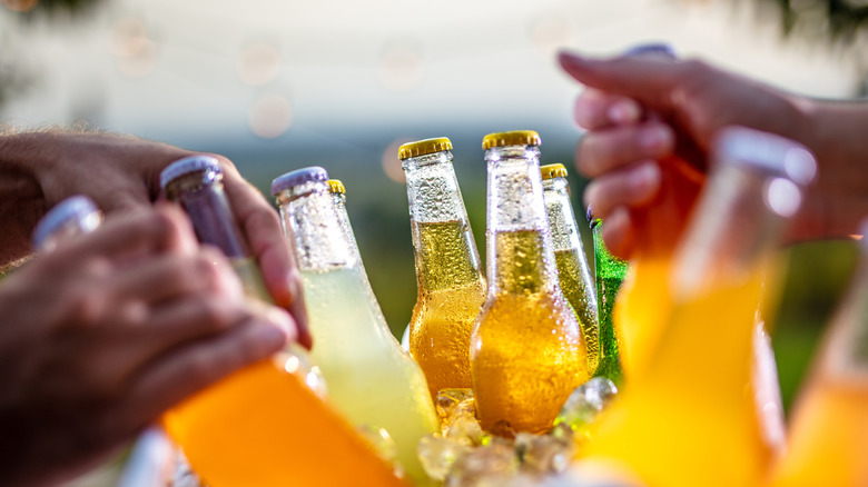 People reaching into a cooler with ice to grab orange colored beverages.