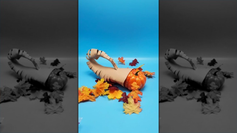 A horn of plenty made of construction paper with faux leaves and a faux pumpkin inside it