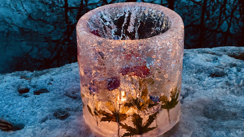 Illuminated ice lantern with leaves sitting on ice and snow