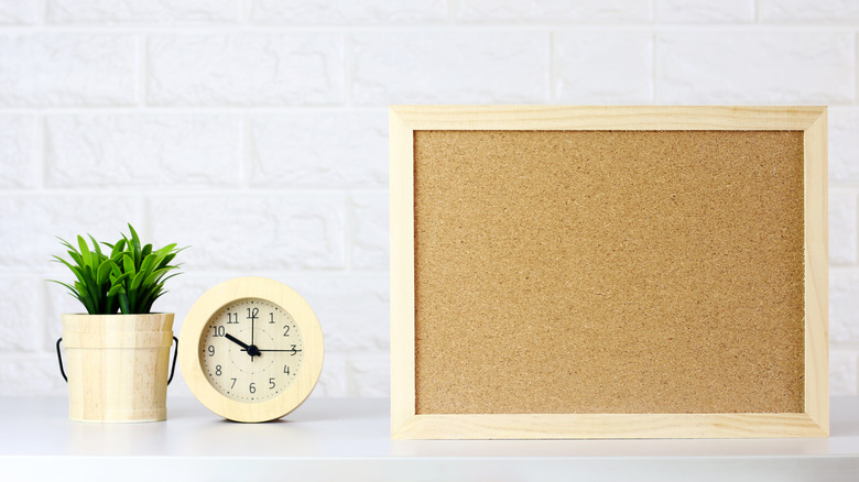 A plain cork board on a kitchen bench with a clock and a small pot plant to the side
