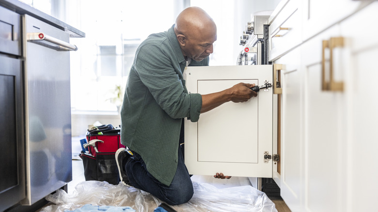 A handyman is installing kitchen cabinet door hinges.