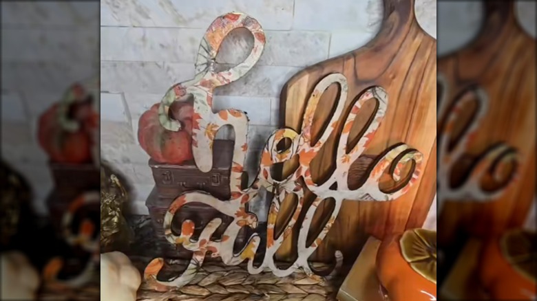 A "hello fall" sign created with a napkin sitting in front of a cutting board and among other fall decorations