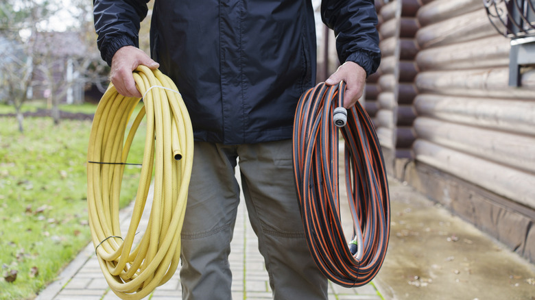 Man holding coiled up garden hoses to store