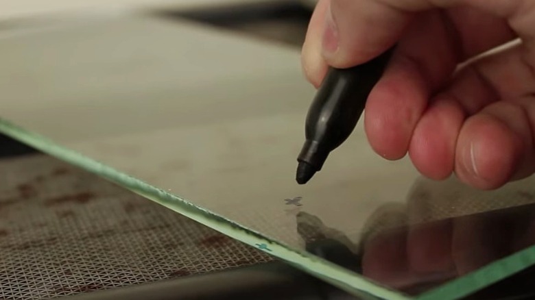 Someone drawing a guide mark on glass before drilling