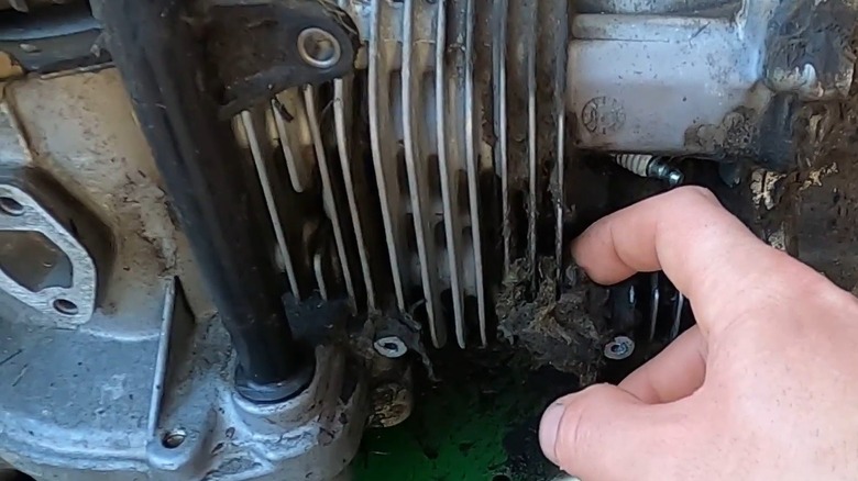 Person removing debris from air fins on a lawn mower engine