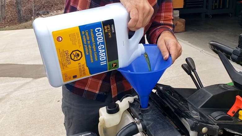 Person adding liquid coolant to a lawn mower engine