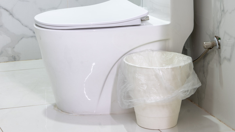 toilet next to white trash bin in marble bathroom