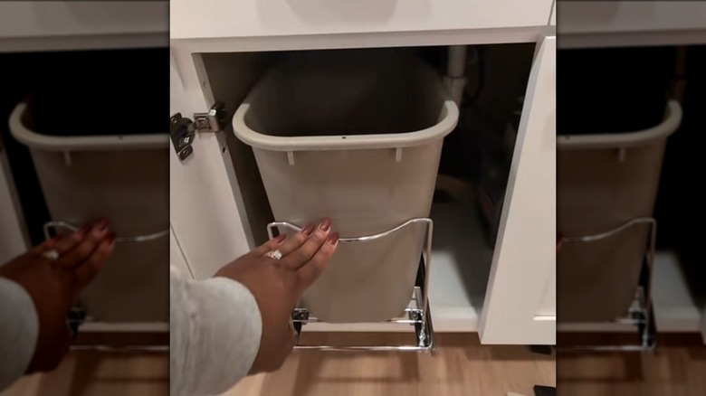 A woman white a ring a brown fingernails pushes in a grey garbage can.