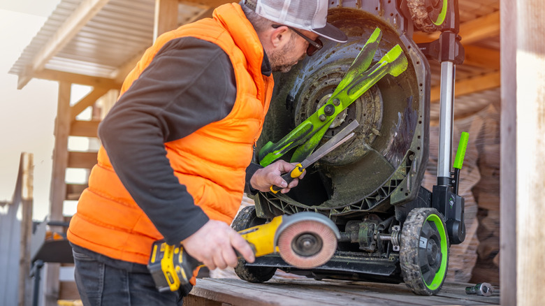 a man inspects lawn mower blades while holding tools to sharpen them