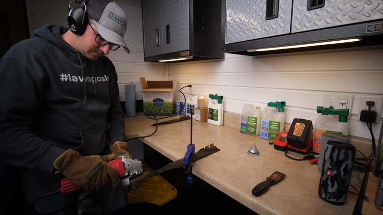 a man sharpens a lawn mower blade with a flap disc on an angle grinder