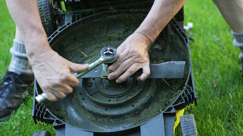 A man uses a work tool to fasten a nut on a battery-powered lawn mower outdoors.