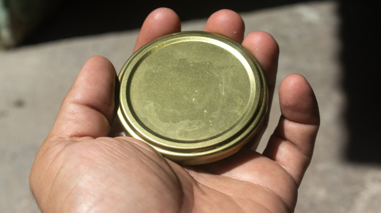 hand holding metal jar lid outdoors in the sum