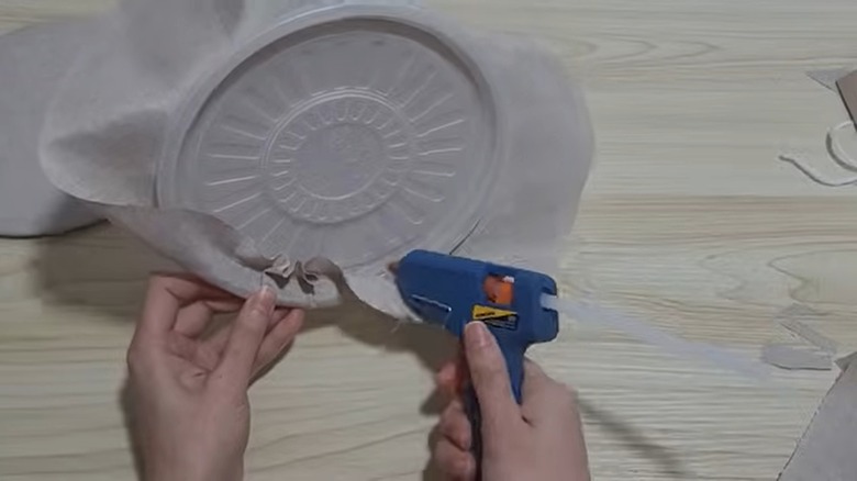 A person gluing fabric to a round plastic lid above a wooden table